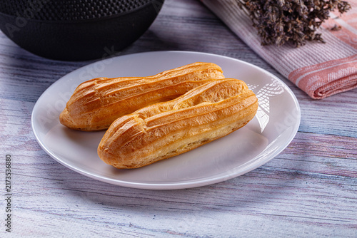 Foto Two golden eclairs on white plate with rustic wooden background