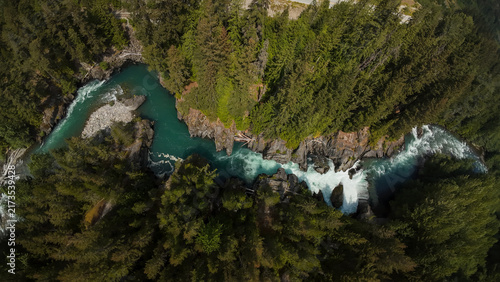 Obraz na plátně A straight top down aerial wide shot overlooks Cheakamus River Waterfalls plunging into a churning rock canyon channel and winding deep within a dense green evergreen forest canopy
