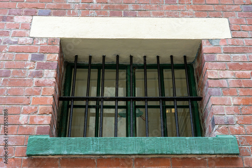 Foto Symmetrical exterior view of vertical black security bars over a green framed window set in a weathered red brick institutional building wall