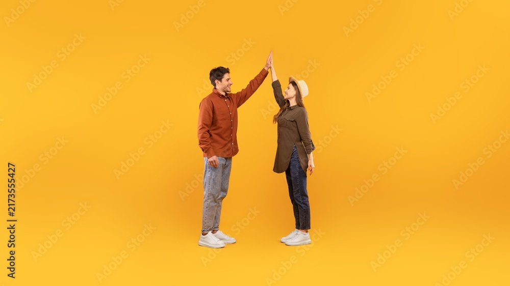 Fototapeta premium Happy Young Man And Woman Engaging In A High Five Gesture, Celebrating A Positive Moment In A Studio With A Yellow Background. Showcasing Joy And Connection, Concept Of Togetherness.