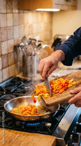 Close-up of hands scraping chopped vegetables from a wooden cutting board into a hot stainless steel pan