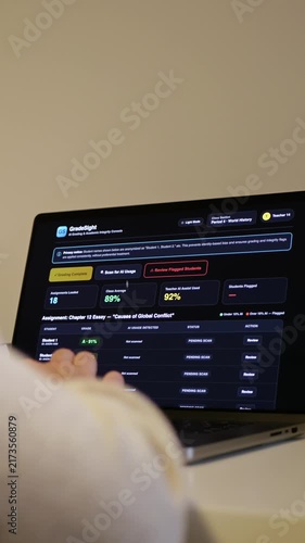 Educator at a laptop using AI software for automated bulk grading of student essays while scanning for unauthorized student AI usage and plagiarism