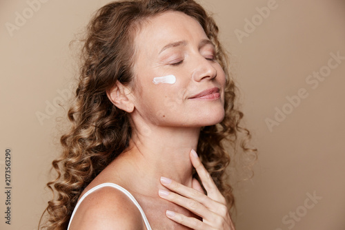 Canvastavla A serene middle aged woman with natural skin applies cream to her cheek, eyes closed, expressing calm