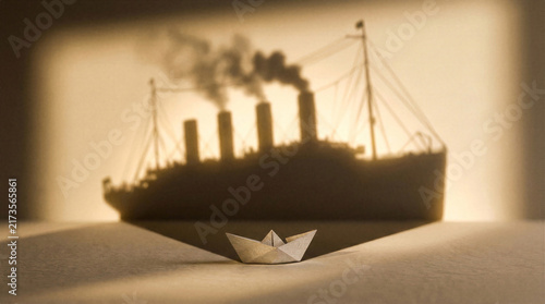 Small origami paper boat casting large shadow of cruise liner representing big potential
