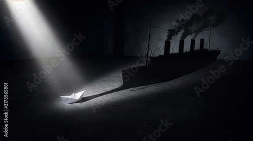 Origami paper boat under spotlight casting shadow of massive steamship representing hidden potential
