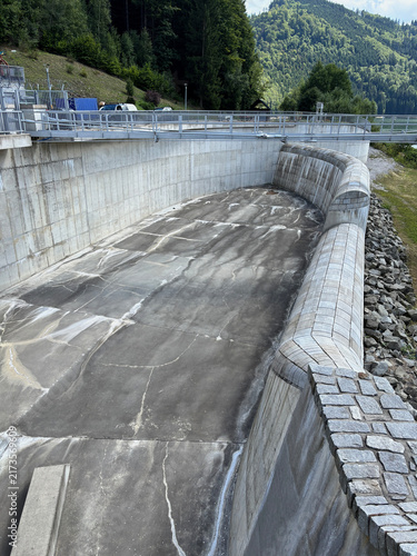 Fotografie Concrete spillway and dam structure with forested mountains.