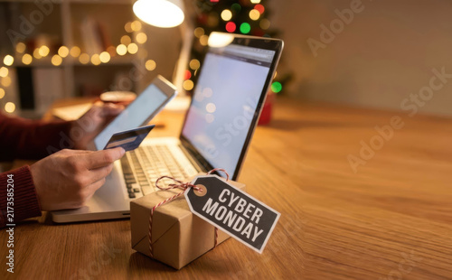 Man shopping online with a credit card during cyber monday sales with a wrapped gift box on a wooden desk
