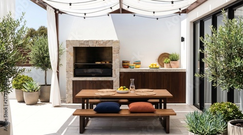 Modern outdoor patio kitchen with built-in stone barbecue, dining table, and pergola for summer entertaining