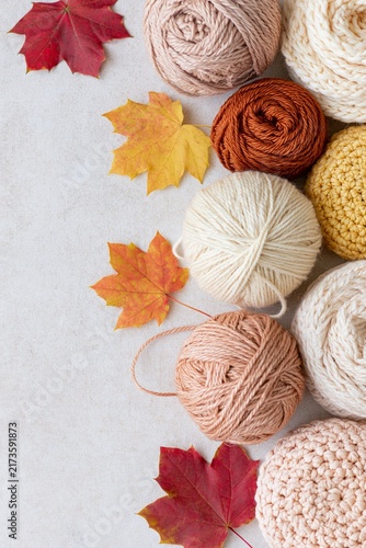 Cozy autumn flat lay with warm neutral yarn balls, knitted textures and colorful maple leaves arranged with copy space