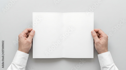 Top Down View of Hands Holding Blank Open Booklet Mockup, Male Businessman in White Shirt Opening a Clean Brochure Template on Gray Background, Minimalist Corporate Stationery Presentation.