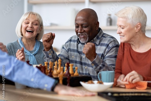 Canvastavla Smiling Senior Group Of Three Members, Mixed Gender And Ethnicity, Playing Chess With Excitement At Cozy Home Setting