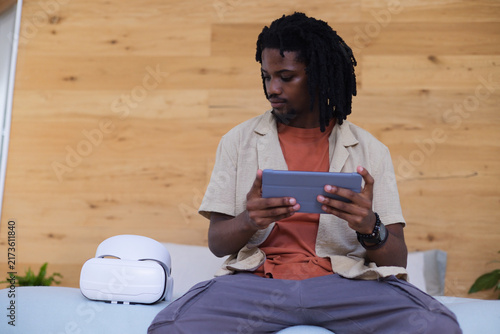 Obraz na płótnie African American man in beige shirt sitting on cushion holding tablet, glancing