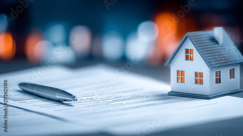 A house model resting on documents beside a pen represents mortgage agreements property purchase and real estate financing.
