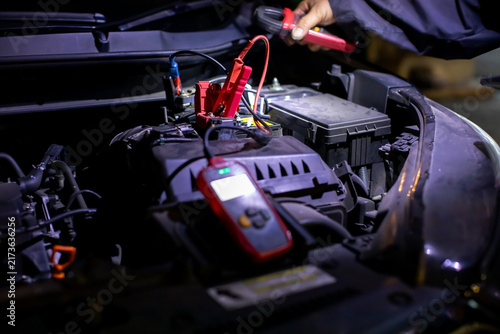 Selective focus to Jumper cable with Professional mechanic performing an on-site diagnostic test on a car battery using a digital tester and clamp meter to check health, voltage, and performance under