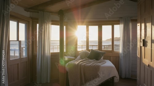 Sunset light streaming into cozy cabin bedroom overlooking ocean waves in this peaceful motion video footage