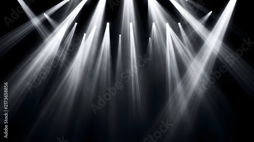 Bright white stage spotlights shining down through darkness creating dramatic light beams.