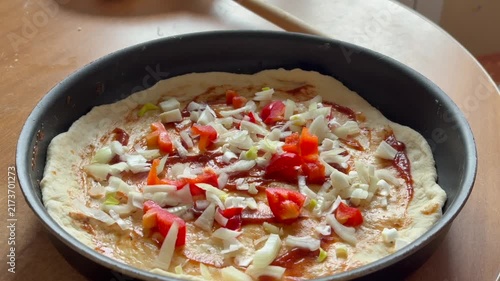 The process of adding ingredients to a raw pizza base with tomato sauce, onions and peppers in a round shape