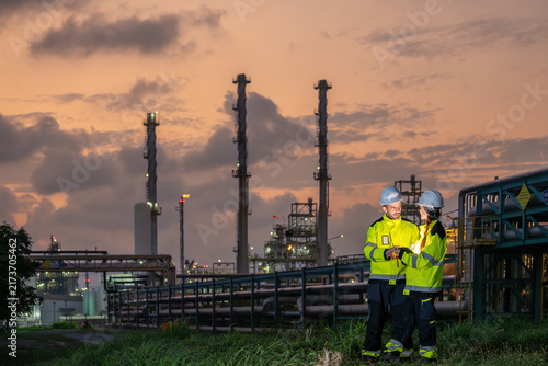 Industrial workers team discussing petroleum engineering in oil refinery project collaboration at fuel industry Male and female engineers using digital tablet at oil refinery site during sunset
