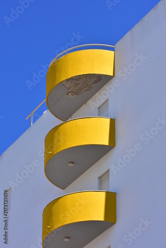 Quadro su tela low-angle architectural shot of a white building featuring a vertical stack of bright yellow, semicircular balconies against a clear blue sky