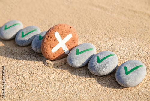 Naklejka Red cross symbol interrupts a row of completed check marks on sand