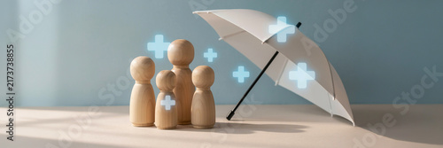 Wooden peg dolls representing a family protected underneath a small white umbrella with umbrella protection insurance security healthcare