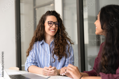 Young adult businesswoman communicating with colleague at professional meeting in corporate office. Smiling female manager provide services  consulting company client sit at desk. Business discussion