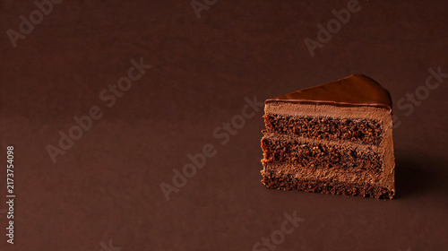 Foto Decadent slice of layered chocolate cake with creamy frosting and rich ganache, presented on a dark brown surface