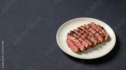 Juicy, perfectly grilled steak, sliced medium-rare, served on a white plate against a dark grey background.