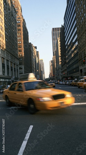 Yellow taxi driving fast on busy city street
