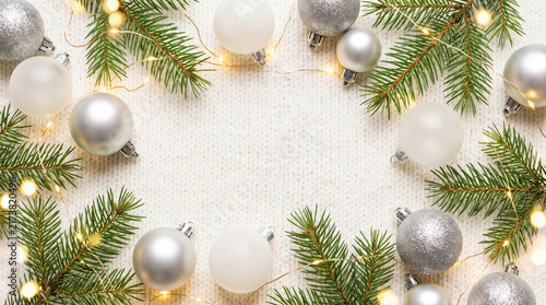 Christmas background with silver baubles and pine branches on white knitted fabric