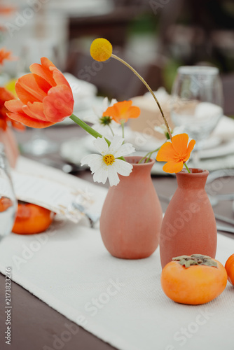 Colorful flowers displayed in small terracotta vases on an elegant table, creating a cheerful floral decoration with a refined event atmosphere.