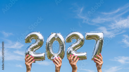 Silver balloons forming the year 2027 held against blue sky