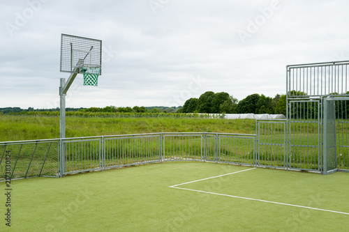 An empty multi-sport court with a basketball hoop on an overcast summer day in Denmark, evoking a quiet, calm, and lonely atmosphere