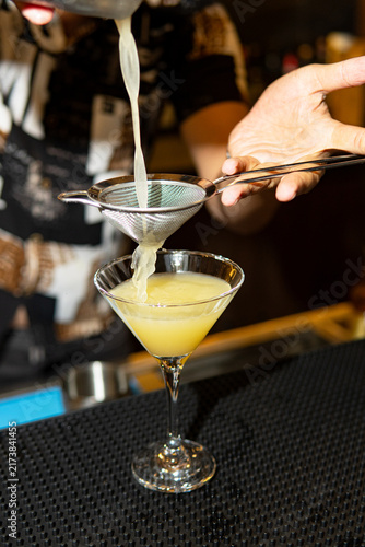 Bartender pouring layered cocktail into martini glass.