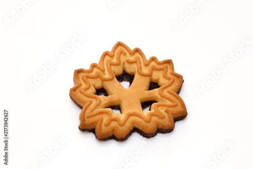 Фотография Golden maple leaf shaped cookie isolated on a clean white background, featuring decorative baked edges, crisp texture, and an autumn seasonal design