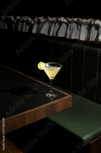 Elegant martini glass with lime on dark booth.