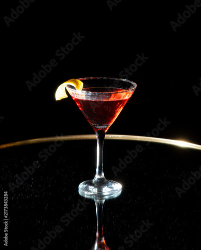 Elegant martini glass with red cocktail and lemon twist.