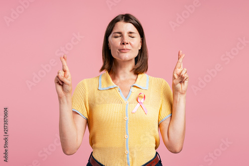 Fotografie Woman wearing pink ribbon crossing fingers wishing hope