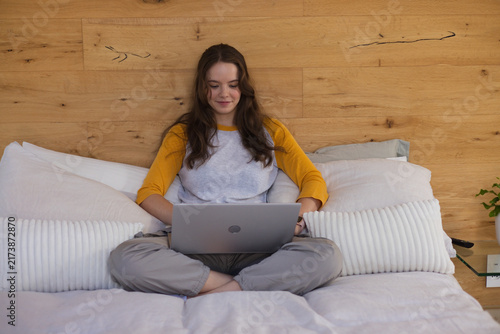 Fotografía Woman sitting cross-legged on bed using silver laptop, wearing grey shirt with y