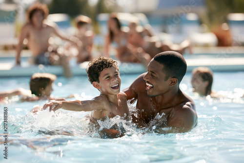 A joyful father and his little son are splashing and laughing together in the outdoor pool.