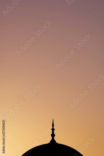 Silhouette of a dome with a pointed finial against a soft sunset sky