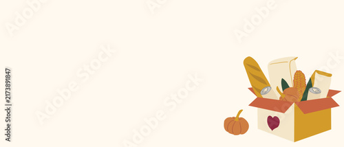 Food donation box with grocery supplies and pumpkin beside wide copy space. Thanksgiving charity banner represents food drive support and community aid