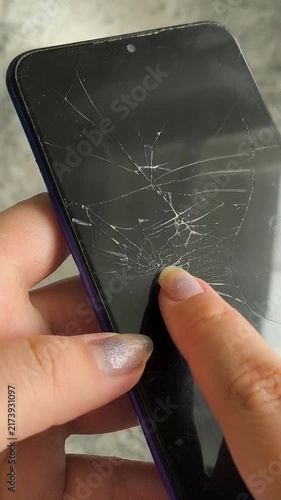 Person holding a smartphone with visible cracks across the touchscreen, broken display, damaged mobile phone and phone repair concept.