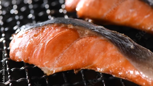 Grilled salmon fillet cooking on a charcoal grill grate, camera zooms in and pans across the seared surface