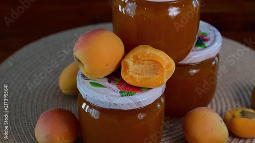 Three glass jars filled with homemade apricot jam are arranged on a woven mat and surrounded by fresh, ripe whole and halved apricots.