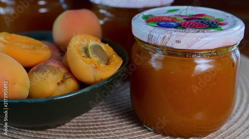 A glass jar of apricot jam sits next to a bowl filled with fresh whole and halved apricots.