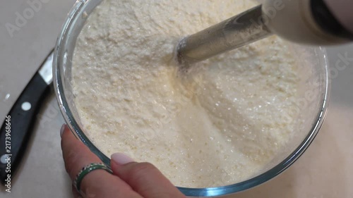 Immersion blender mixing cottage cheese in a glass bowl. Static top-down shot of kitchen food preparation.