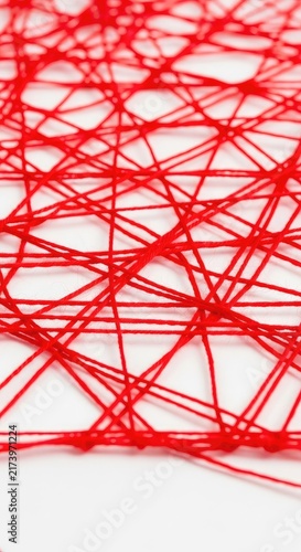 A detailed web of bright red yarn forms a complex geometric pattern against a clean white surface, showcasing delicate fibers and textures, white, filament, geometric