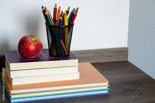 Obraz na płótnie Stack of books with red apple and colored pencils in holder on wooden desk for e