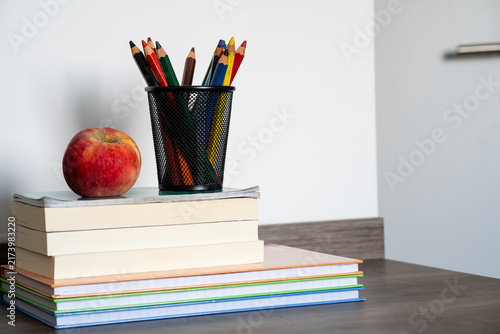 Fotografía Stack of books with red apple and colored pencils in holder on wooden desk for e